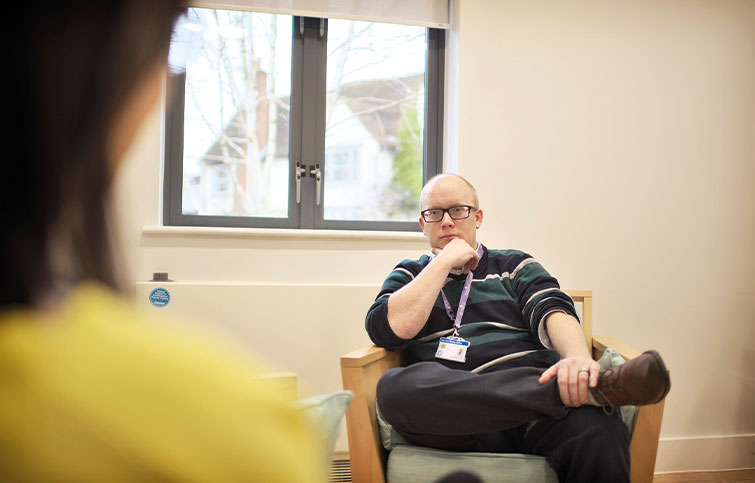 A male counsellor is listening to another person, the image is taken from over their shoulder.