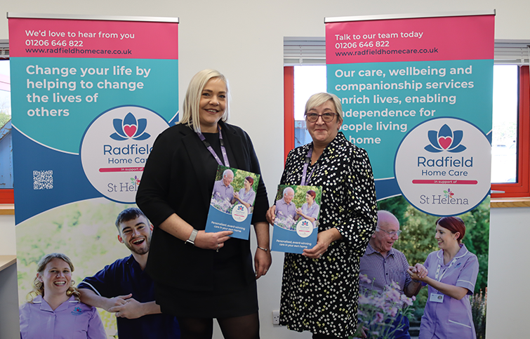 two women holding posters for Radfield Home Care in support of St Helena in front of 2 large banners advertising the service