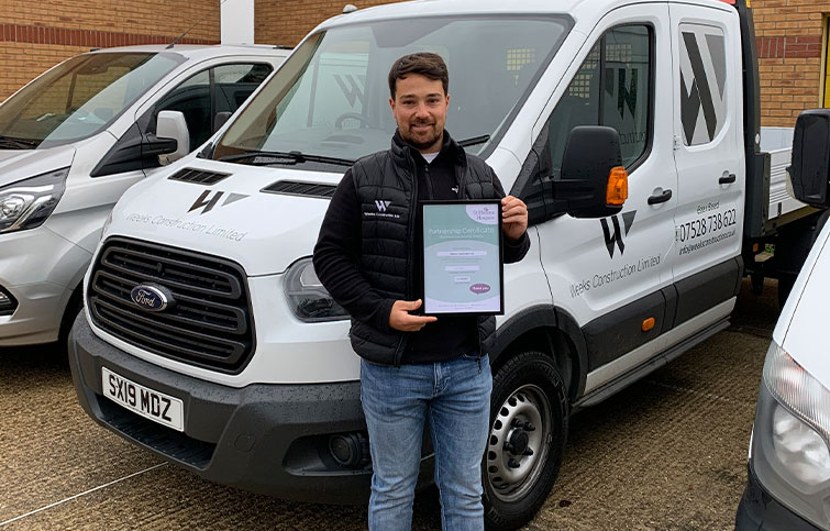 Ryan Weeks, managing director of Weeks Construction holding a Corporate Membership Scheme certificate in front of a van.